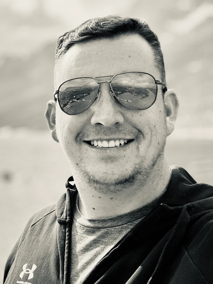 Brandon Gee, smiling outdoors in aviator sunglasses.